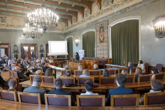 Konferencja w sali obrad z uczestnikami i prezentacją na ekranie.