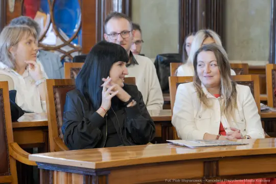 Dwie kobiety rozmawiają w sali z innymi uczestnikami spotkania.