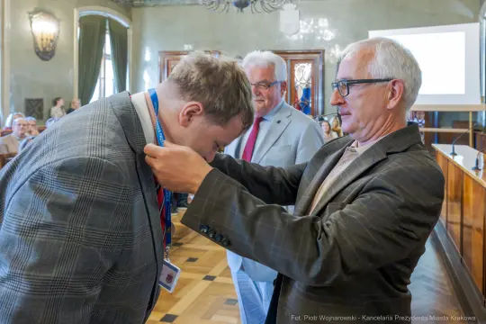 Mężczyzna otrzymuje medal od innego mężczyzny w formalnym otoczeniu.