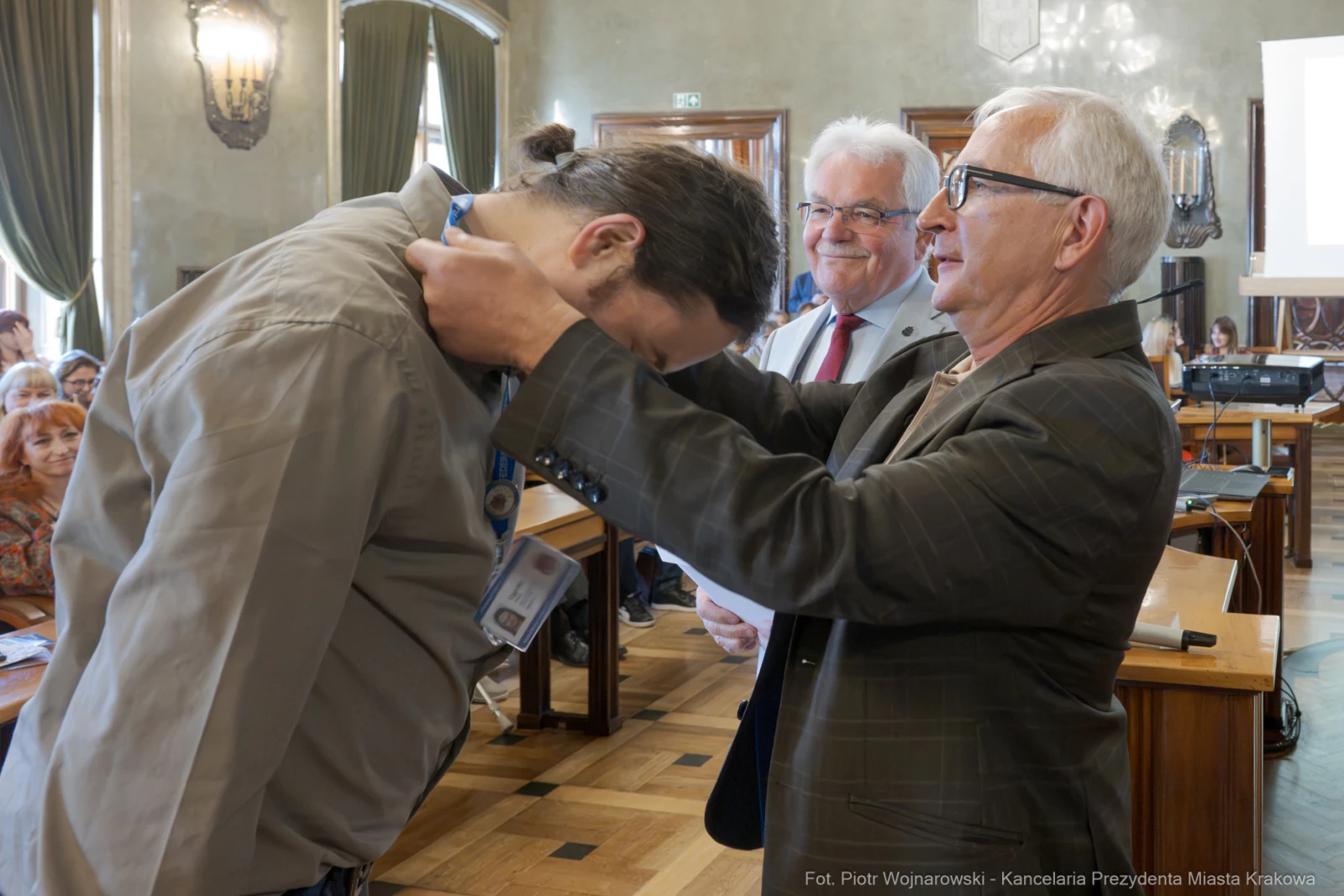 Mężczyzna odbiera medal od innego mężczyzny w obecności grupy ludzi.  Autor: Piotr Wojnarowski