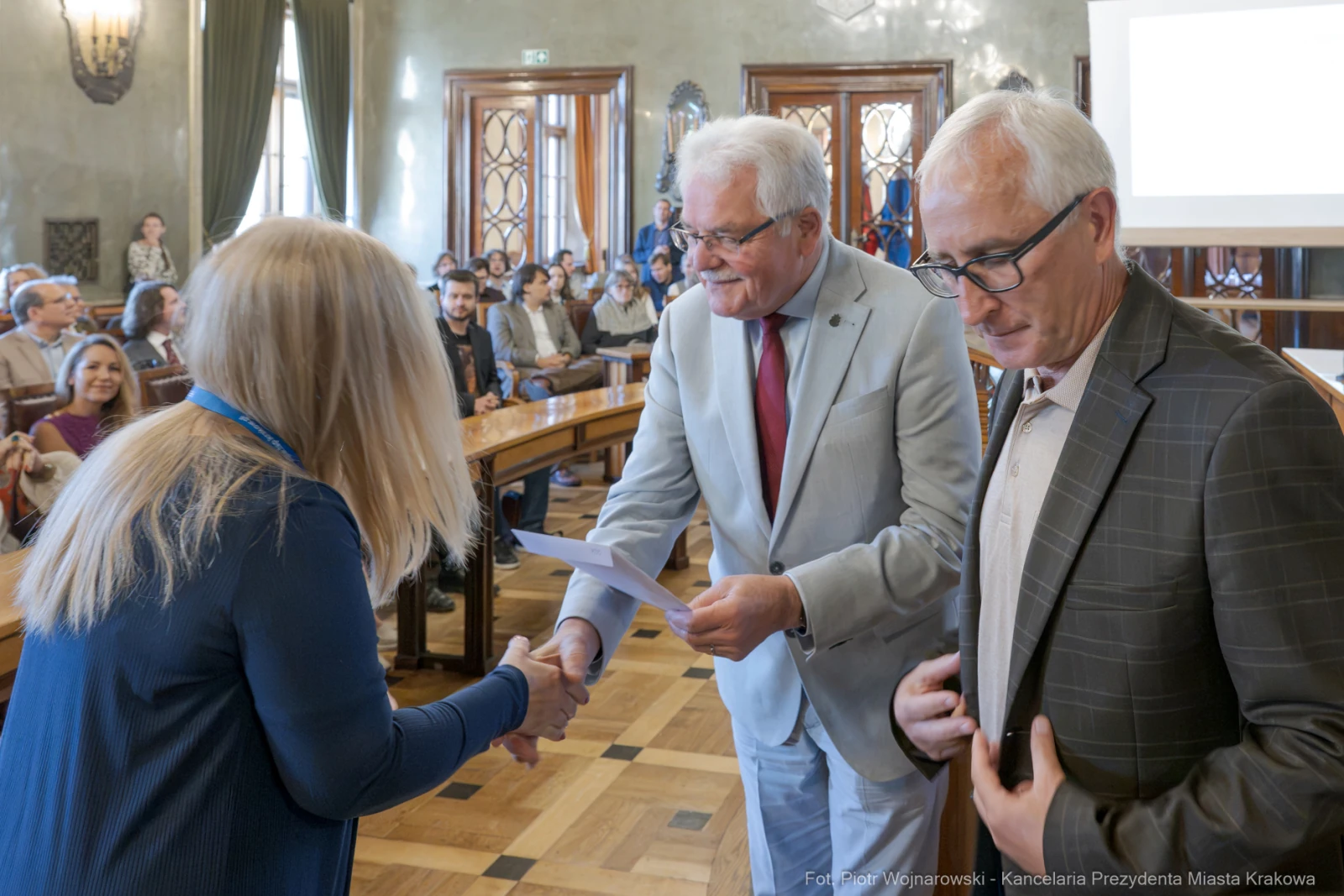 Wręczenie nagrody podczas uroczystości w sali obrad z uczestnikami w tle.  Autor: Piotr Wojnarowski