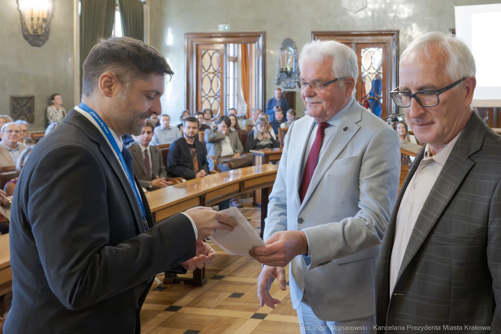 Wręczenie nagrody w sali obrad z udziałem trzech mężczyzn i publiczności.  Autor: Piotr Wojnarowski