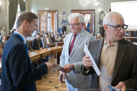 Wręczenie nagród w sali obrad, uczestnicy w formalnych strojach.