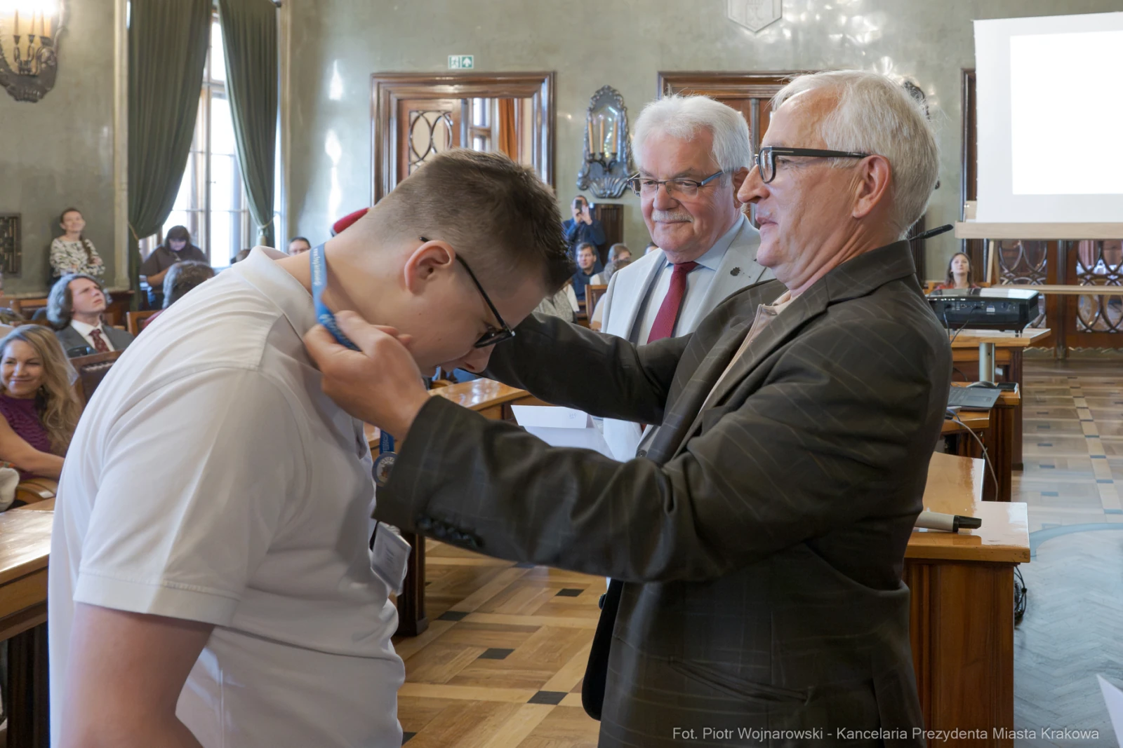 Wręczenie nagrody młodemu uczestnikowi przez dwóch mężczyzn w sali obrad.  Autor: Piotr Wojnarowski