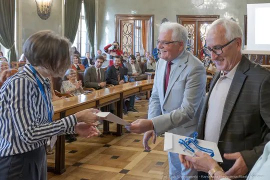 Wręczenie nagród podczas uroczystości w sali obrad z uśmiechniętymi uczestnikami.