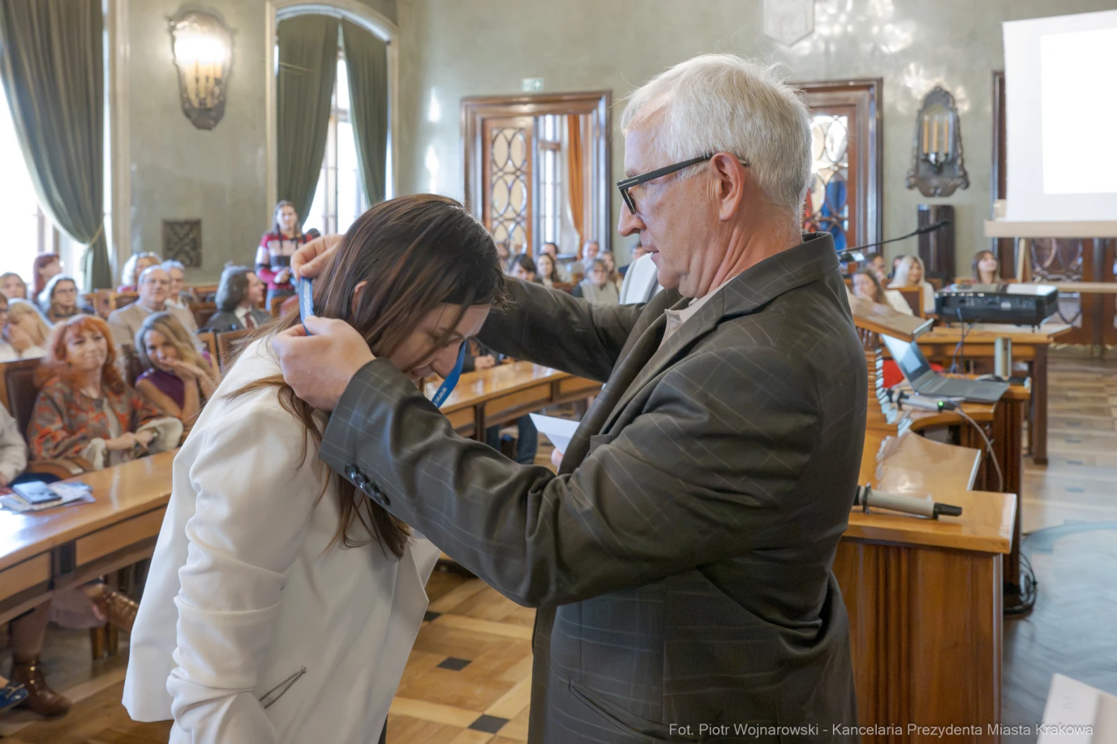 Wręczenie medalu podczas ceremonii w sali obrad z uczestnikami w tle.  Autor: Piotr Wojnarowski