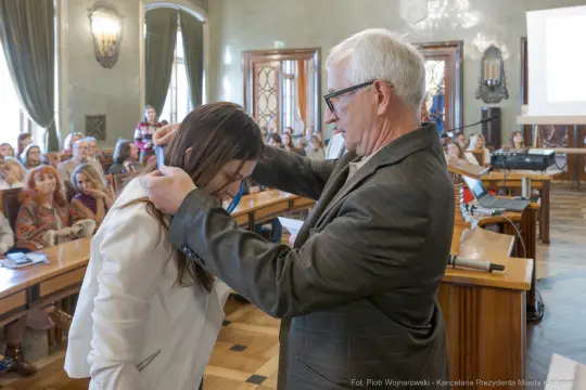 Wręczenie medalu podczas ceremonii w sali obrad z uczestnikami w tle.