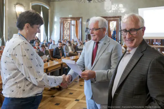 Wręczenie nagrody podczas uroczystości w sali obrad z uczestnikami w tle.
