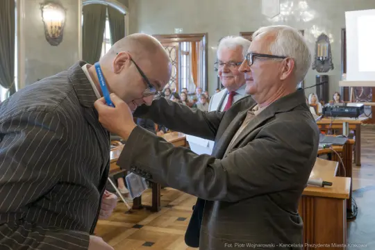 Mężczyzna odbiera medal w sali obrad, w tle widoczni inni uczestnicy wydarzenia.