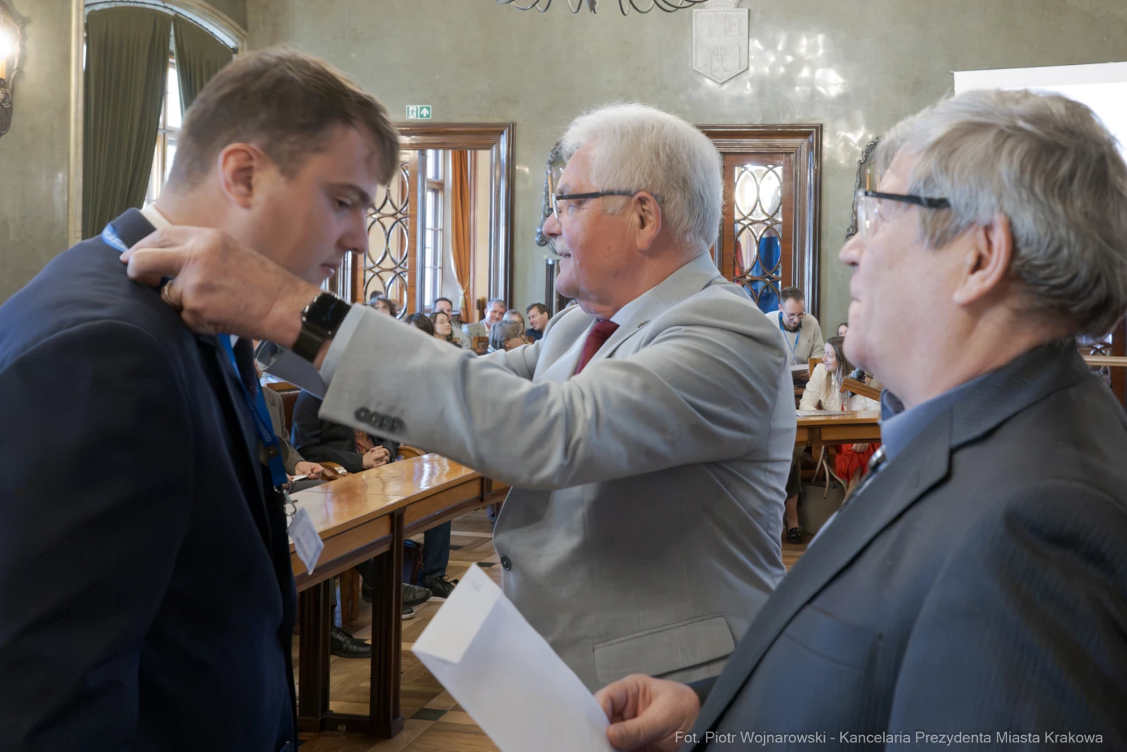 Ceremonia wręczenia odznaczenia w sali obrad z udziałem trzech mężczyzn.  Autor: Piotr Wojnarowski