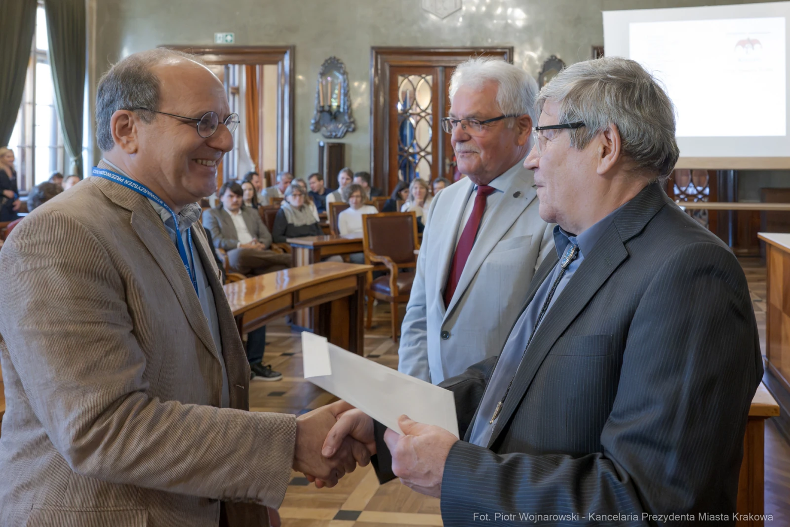 Mężczyźni w garniturach wymieniają uściski dłoni i dokumenty w sali konferencyjnej.  Autor: Piotr Wojnarowski