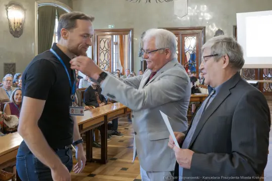 Ceremonia wręczenia nagrody, mężczyzna odbiera medal od dwóch innych mężczyzn.