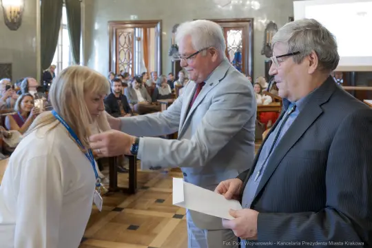 Wręczenie nagrody przez dwóch mężczyzn kobiecie podczas uroczystości w sali.
