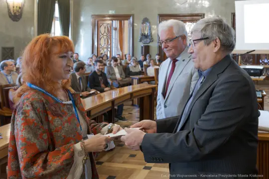 Wręczenie nagrody w sali obrad z uczestnikami w tle.