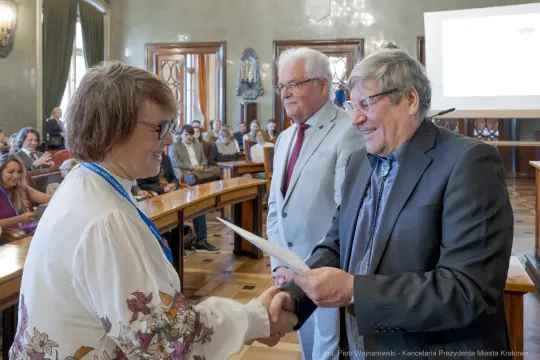 Wręczenie nagrody podczas uroczystości w sali obrad z uczestnikami w tle.