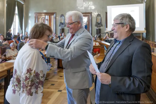 Wręczenie nagrody podczas uroczystości w sali obrad z uczestnikami w tle.