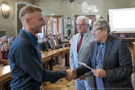 Mężczyzna odbierający nagrodę w sali obrad, w tle zgromadzeni goście.
