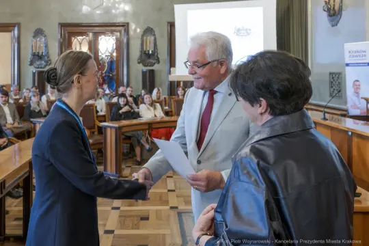 Wręczenie nagrody w sali obrad, uściski dłoni i uśmiechy uczestników.