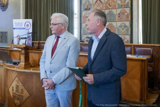 Dwóch mężczyzn w formalnych strojach podczas wydarzenia w sali konferencyjnej.