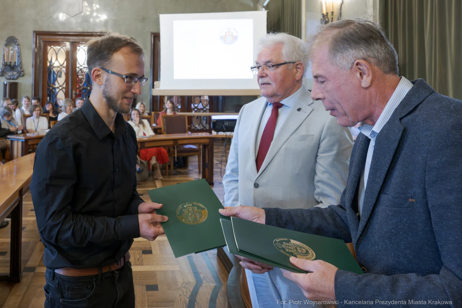 Wręczenie dokumentów w sali obrad, trzech mężczyzn w formalnych strojach.  Autor: Piotr Wojnarowski