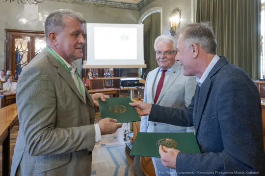 Trzech mężczyzn wymienia dokumenty w sali konferencyjnej.