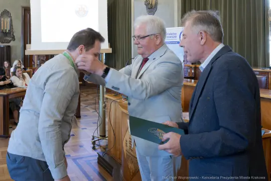 Wręczenie medalu przez mężczyznę w garniturze, uhonorowanie innego mężczyzny.