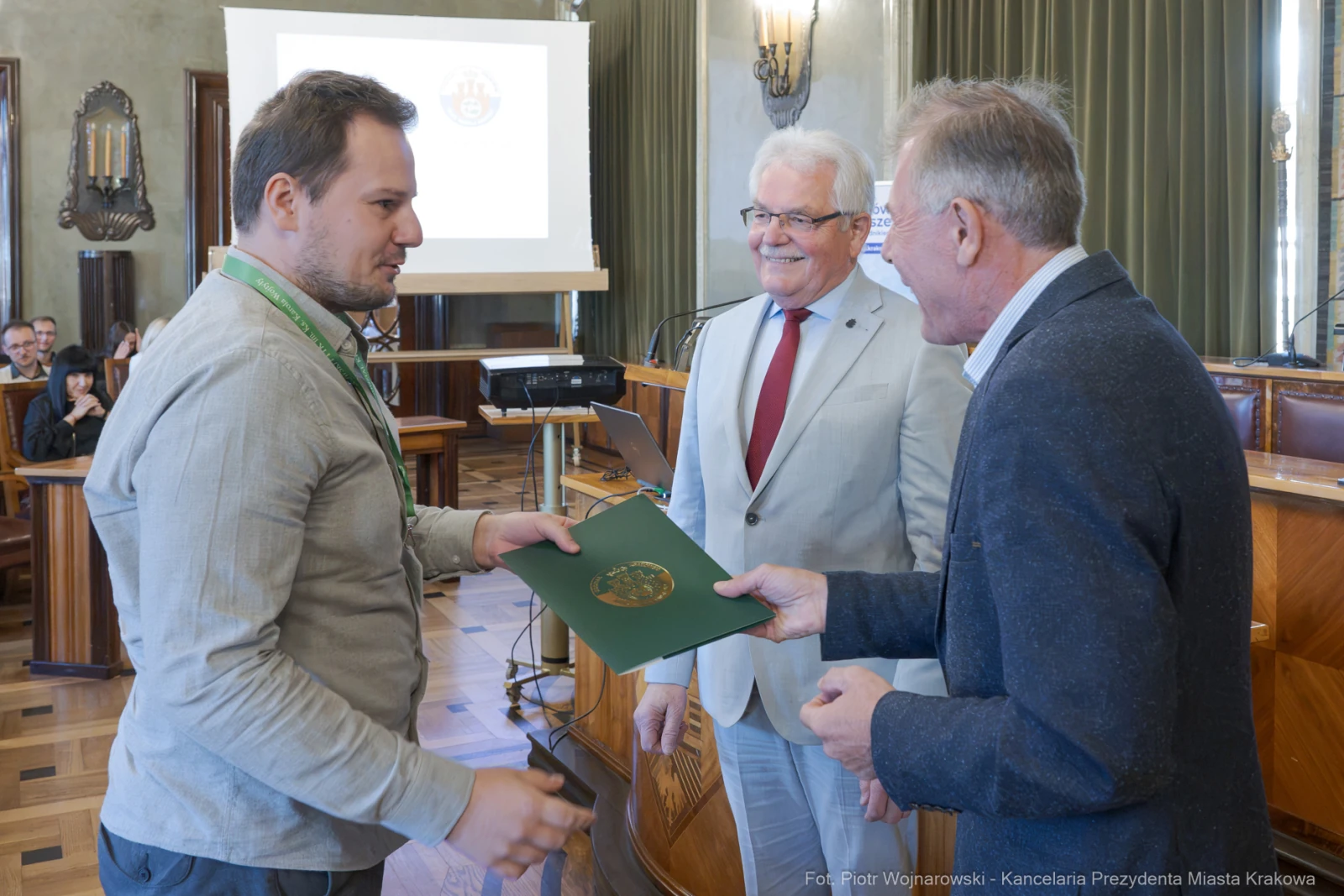 Wręczenie dyplomu lub nagrody w sali konferencyjnej. Uczestnicy uśmiechnięci.  Autor: Piotr Wojnarowski