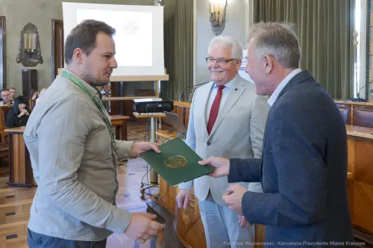 Wręczenie dyplomu lub nagrody w sali konferencyjnej. Uczestnicy uśmiechnięci.