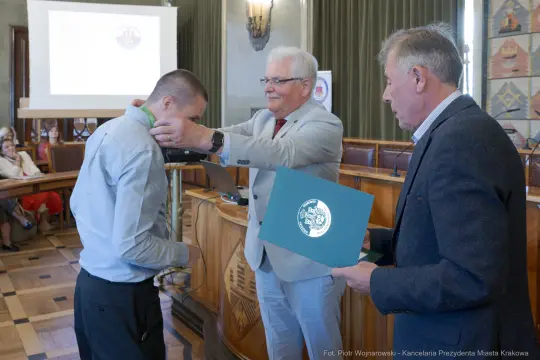 Wręczenie nagrody przez mężczyznę w garniturze młodemu mężczyźnie w koszuli.