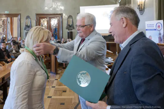 Wręczenie odznaczenia przez mężczyznę kobiecie w sali z publicznością.