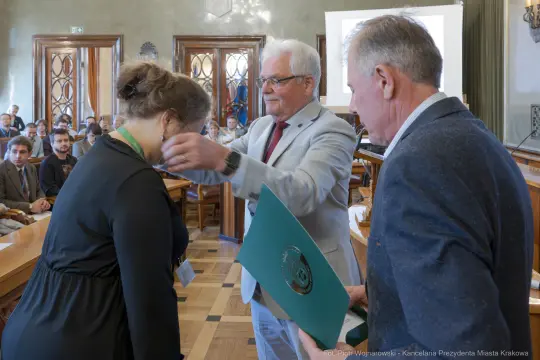 Wręczenie nagrody przez mężczyznę w garniturze kobiecie z medalem na szyi.