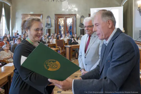 Wręczenie dyplomu w sali obrad z udziałem trzech osób.