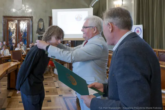 Wręczenie dyplomu młodemu laureatowi w sali obrad.