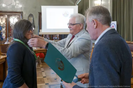 Wręczenie medalu honorowego przez mężczyznę kobiecie w sali obrad.