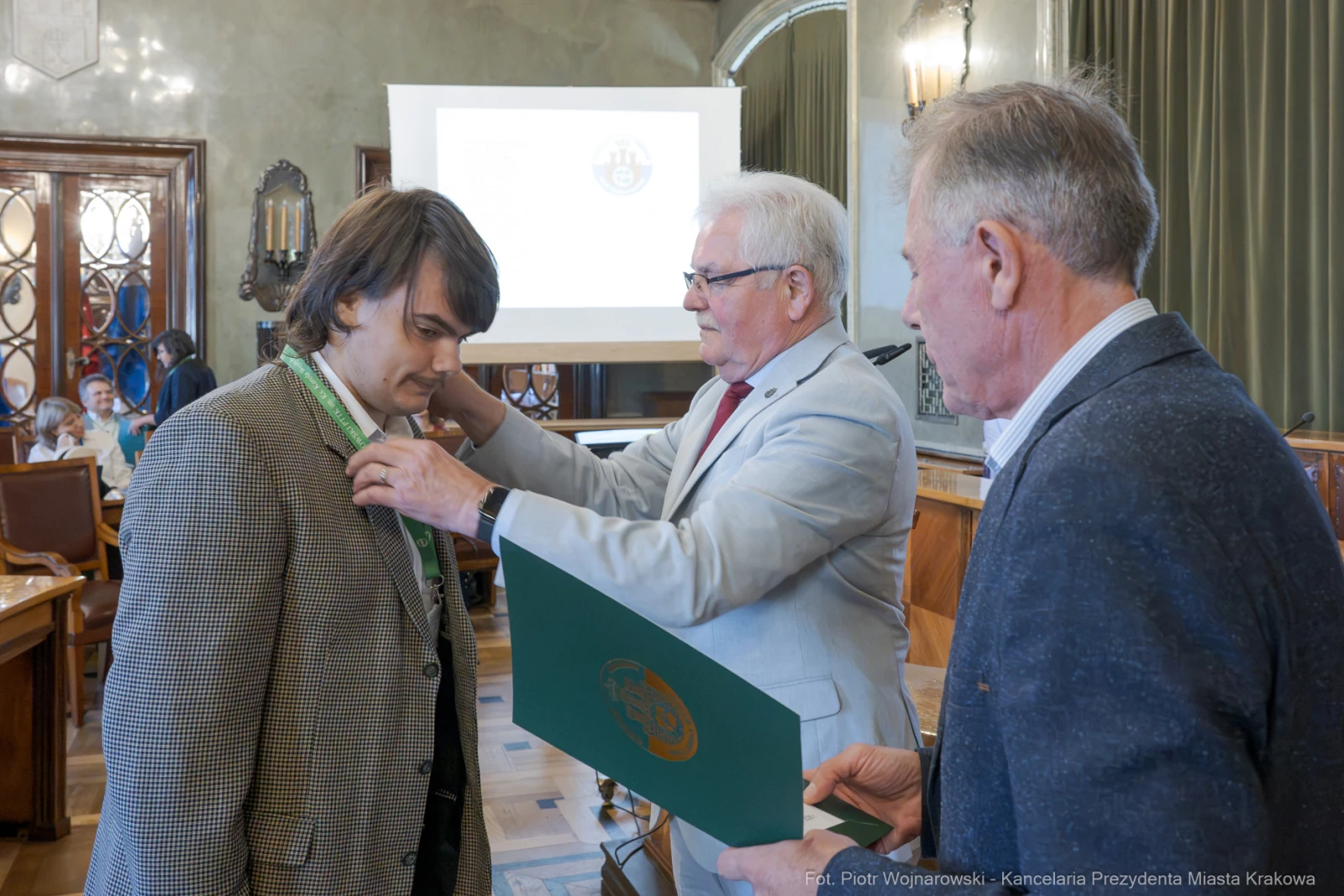 Mężczyzna otrzymuje medal od innego mężczyzny w formalnym otoczeniu.  Autor: Piotr Wojnarowski