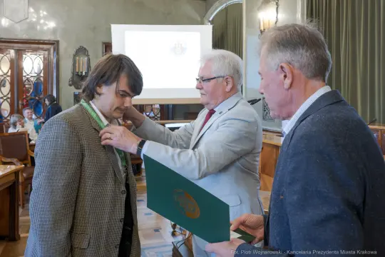 Mężczyzna otrzymuje medal od innego mężczyzny w formalnym otoczeniu.