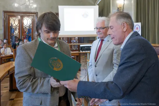 Mężczyzna odbierający dyplom w sali obrad z obecnością innych osób.