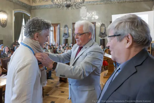 Ceremonia wręczenia odznaczenia w sali obrad z uczestnikami w tle.