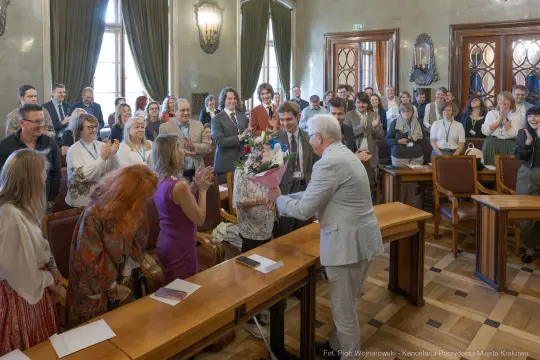 Uroczystość wręczenia kwiatów w sali obrad z uczestnikami w tle.