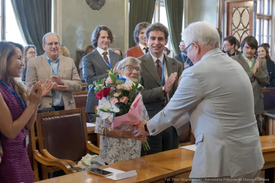Kobieta otrzymuje bukiet kwiatów, otoczona przez uśmiechających się ludzi.