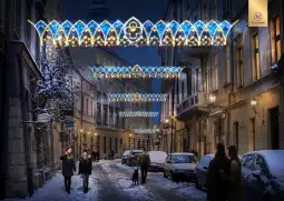 Ulica z ozdobami świetlnymi w zimowej scenerii, ludzie spacerują wśród śniegu.