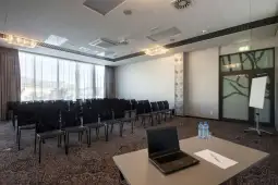 Pusty pokój konferencyjny z krzesłami, stołem, laptopem i butelkami wody.