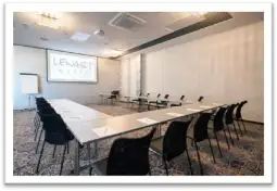 Sala konferencyjna z długim stołem, krzesłami i ekranem projekcyjnym.
