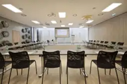 Sala konferencyjna z okrągłym układem stołów i krzeseł, ekranem prezentacyjnym.