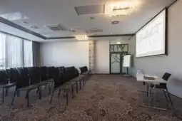 Sala konferencyjna z rzędem krzeseł, ekranem i flipchartem.