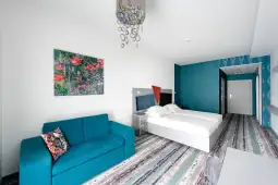 Nowoczesny pokój hotelowy z niebieską sofą, dużym łóżkiem i kolorowym obrazem na ścianie.