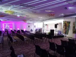Sala konferencyjna z oświetleniem, stołami i ekranem prezentacyjnym.