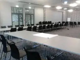 Pusty pokój konferencyjny z dużymi stołami i krzesłami.