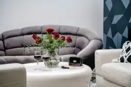 Czerwone róże w wazonie, dwa kieliszki wina i torebka na białym stole w nowoczesnym salonie.