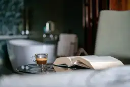 Kawa w filiżance obok otwartej książki na stoliku w łazience.